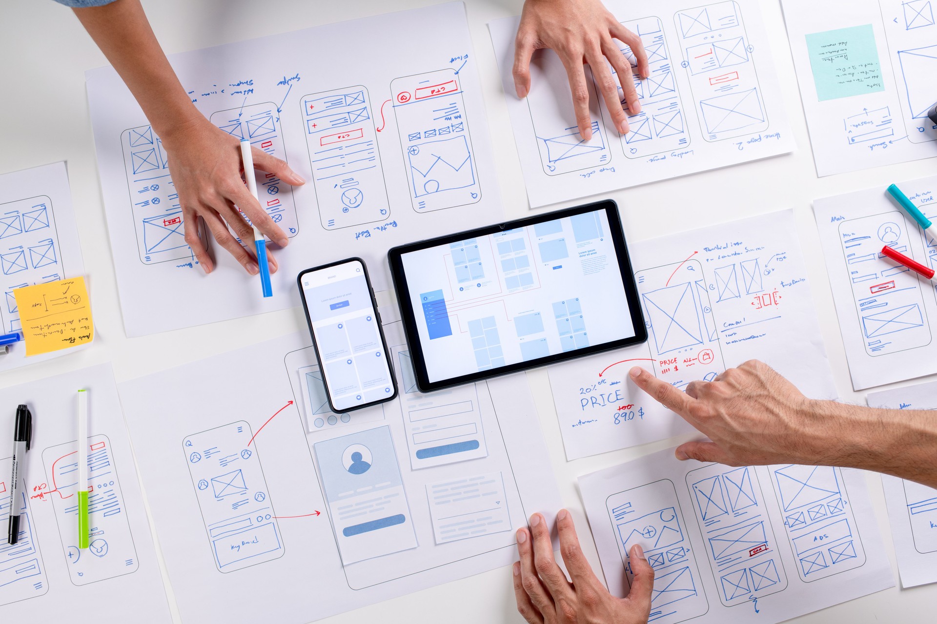 UX/UI designers discussing and brainstorming on wireframes for a website and mobile app prototype, surrounded by sketches of user flow and design tools, in the concept of website and mobile application design concept.